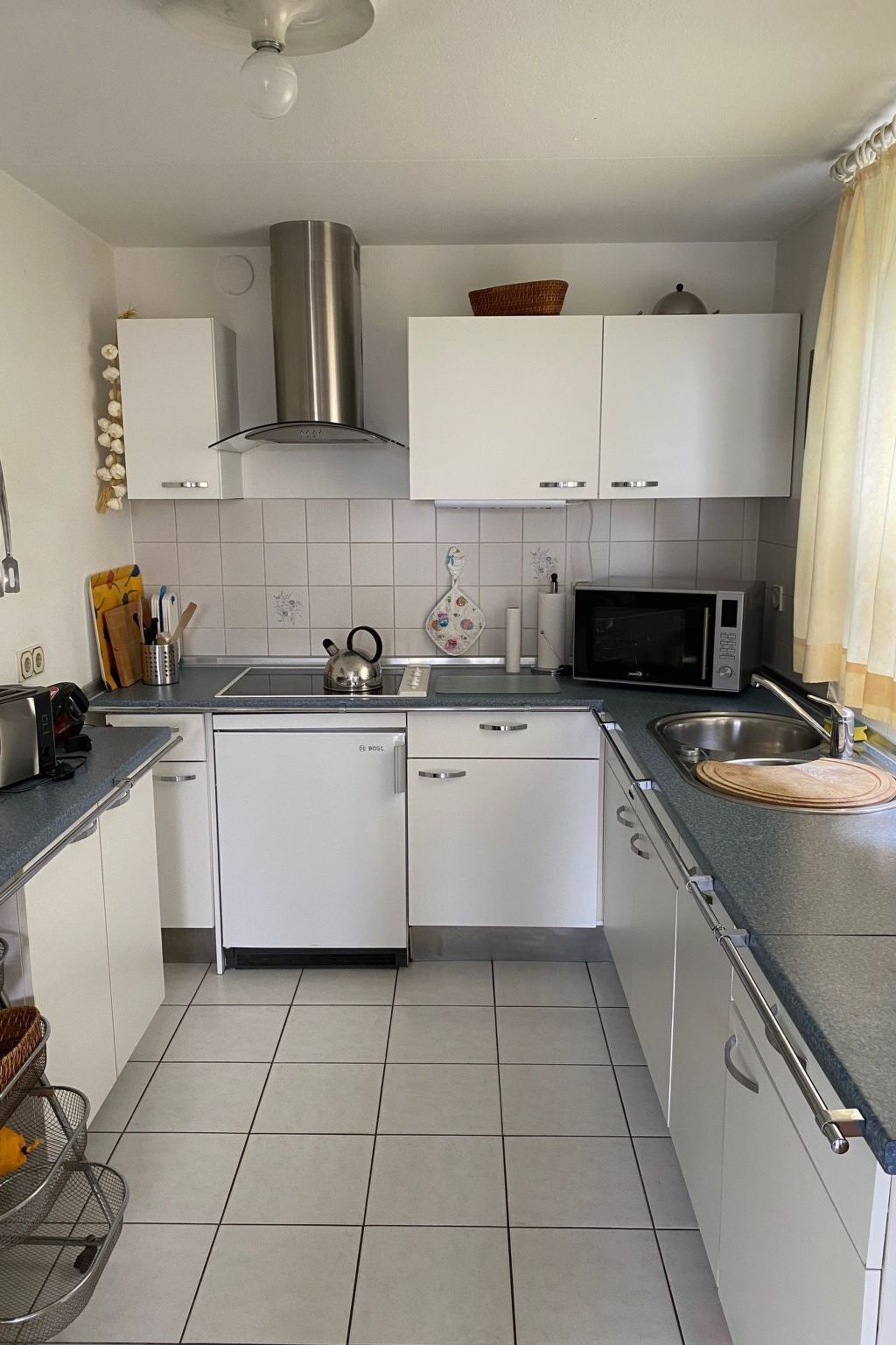 Eine moderne Küche mit weißen Schränken, einer Edelstahl-Dunstabzugshaube, einem Geschirrspüler von Bosch, einer Mikrowelle und einem Spülbecken.