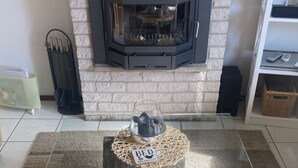 Un salon avec une cheminée, une petite table ronde sur laquelle est posée une pancarte indiquant « CHAMBRES D’HÔTES ET PETIT-DÉJEUNER », et trois bougies sur un plateau en osier.