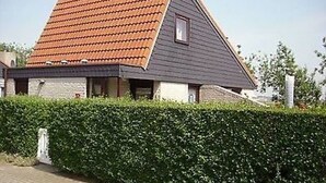 Une maison avec un toit en pente, une petite fenêtre et une haie devant.