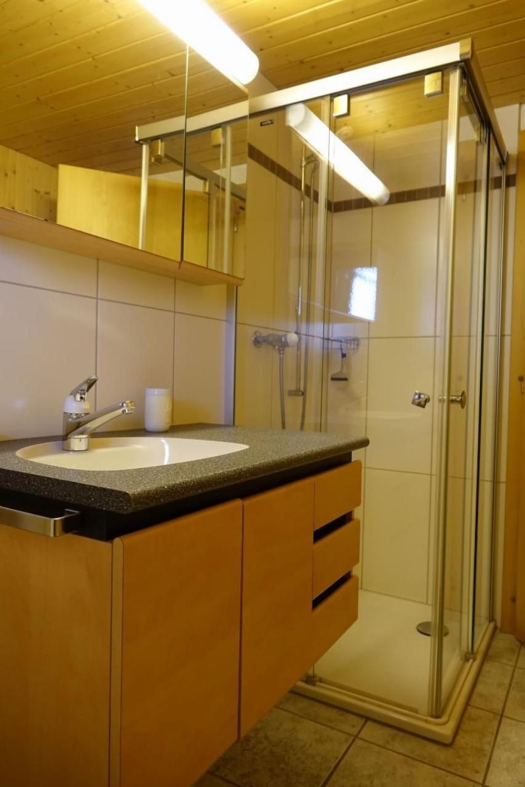 A modern bathroom with a glass-enclosed shower, a sink with a granite countertop, and wooden cabinetry.