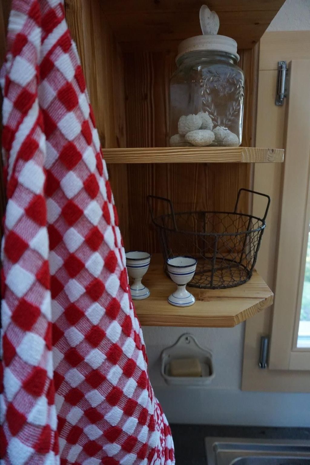 A kitchen shelf with a jar, a wire basket, and two bowls.