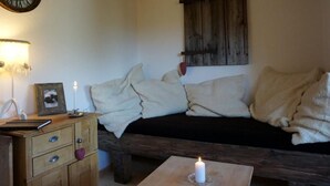 Une pièce chaleureuse avec un banc en bois, une horloge murale, un tableau encadré et une bougie allumée sur une table.