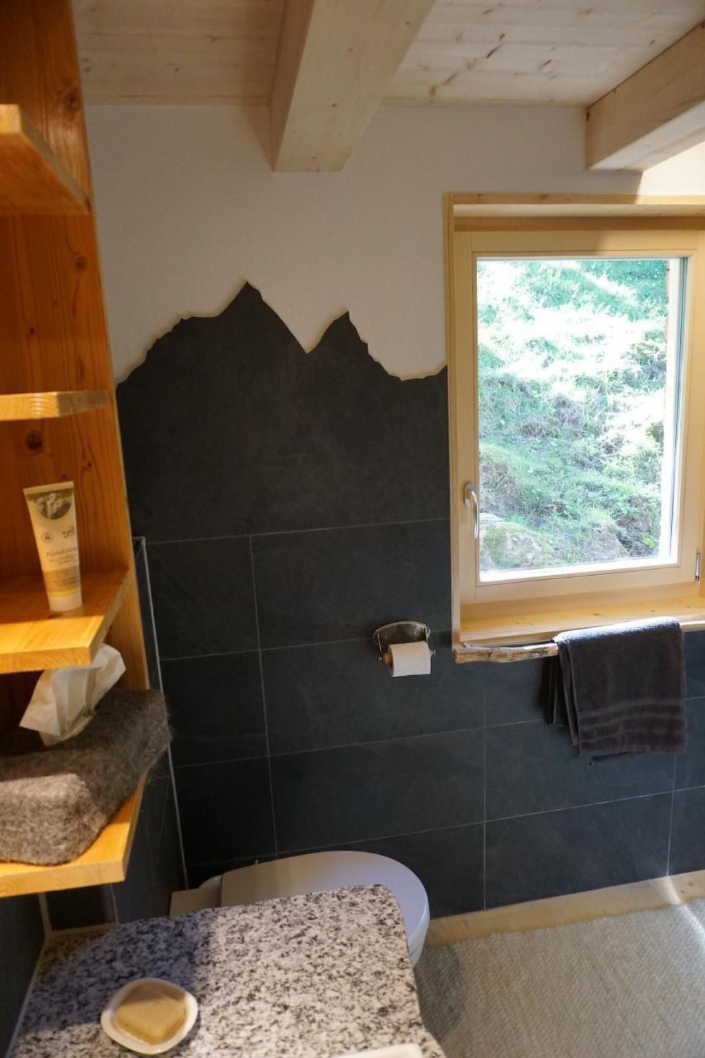 Een badkamer met een houten plank, een handdoekhouder, een raam en een wastafel met een granieten blad.