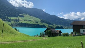 Paisaje rural con un lago, montañas y una casa pequeña con un camino que la lleva a ella.