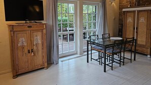 Ein Essbereich mit Tisch und Stühlen, einem Fernseher auf einer Holzkommode und einem großen Fenster mit Vorhängen.