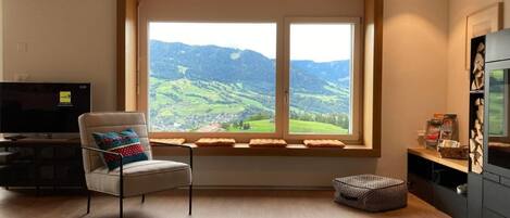 Una sala de estar moderna con un ventanal que ofrece una vista panorámica de colinas verdes.