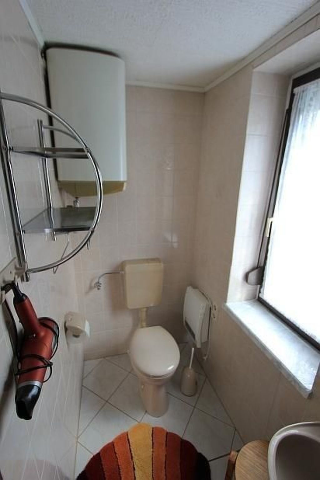 Et lille badeværelse med toilet, bruser og et vindue.