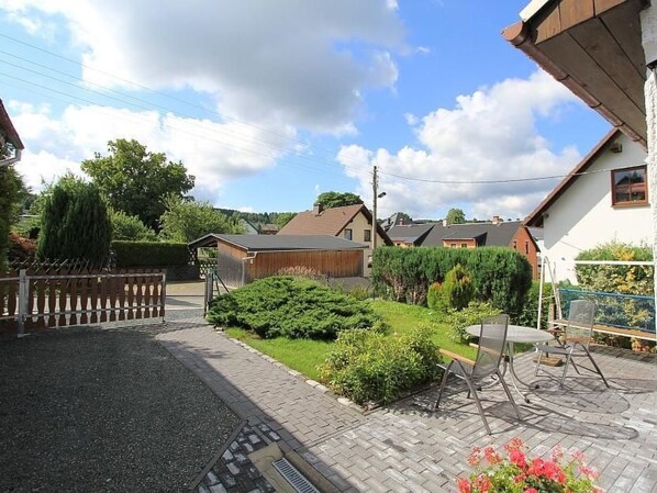 A residential area with a paved driveway, a wooden fence, and a garden with a table and chairs. - Martina by Interhome (Auerbach)