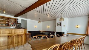 Een ruime eethoek met een lange houten tafel en bijpassende stoelen, een bar met barkrukken en een gezellige zithoek met een bank en kussens.