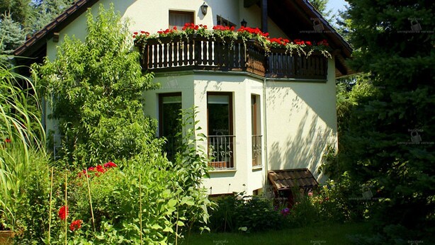 A two-story house with a balcony adorned with red flowers, surrounded by lush greenery. - Fewo Ginkgo II by Interhome (Dresden)