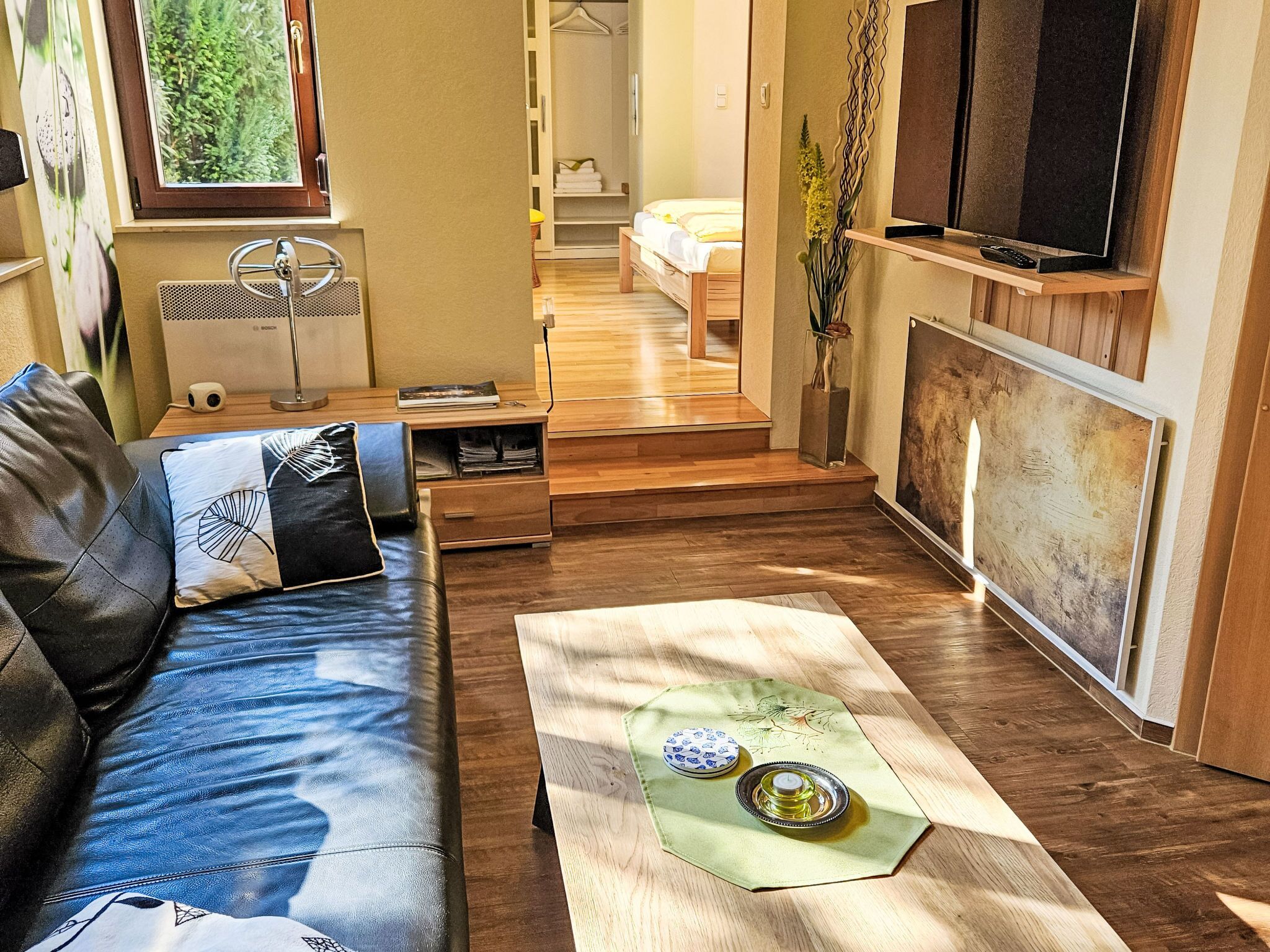 Una sala de estar moderna con un sofá, una mesa de centro con adornos, un televisor y un pasillo que lleva a un dormitorio.