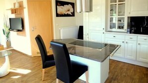 A modern kitchen with white cabinets, a glass island, and a black chair. - Fewo Ginkgo II by Interhome (Dresden)