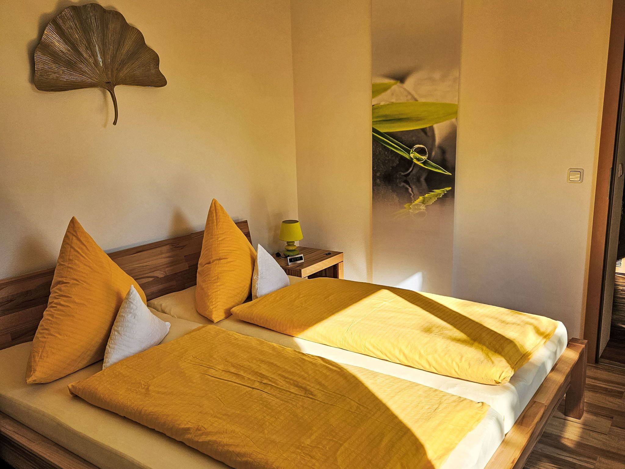 A double bed with two pillows, a bedside table with a lamp, and a wall-mounted decorative item.