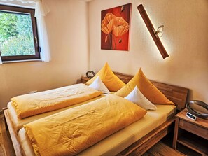 A double bed with yellow bedding, a wooden headboard, a bedside table with a lamp, and a window with curtains. - Fewo Ginkgo by Interhome (Dresden)
