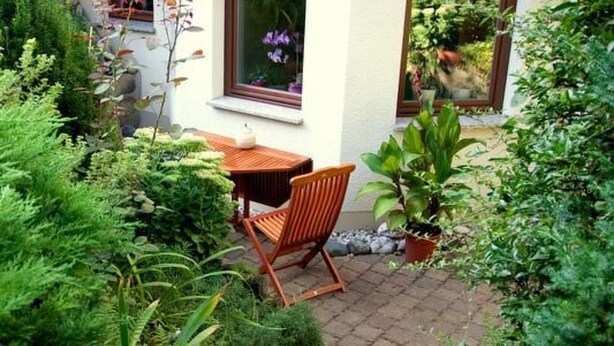 Eine Terrasse mit Holztisch und Stuhl, umgeben von üppiger Bepflanzung und Topfpflanzen.