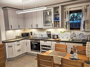 A modern kitchen with white cabinets, a microwave, an oven, a sink, and a dining area with a table and chairs. - Fewo Ginkgo by Interhome (Dresden)