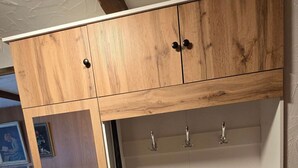Un armario de madera con varios compartimentos y ganchos, una silla y un cuadro en la pared.