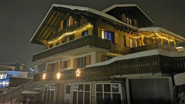 Un edificio de madera de varios pisos con balcones y luces colgantes, que cuenta con un espacio al aire libre cubierto y una entrada visible.