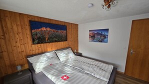 Un dormitorio con cama, mesita de noche, lámpara, dos cuadros y una puerta de madera.