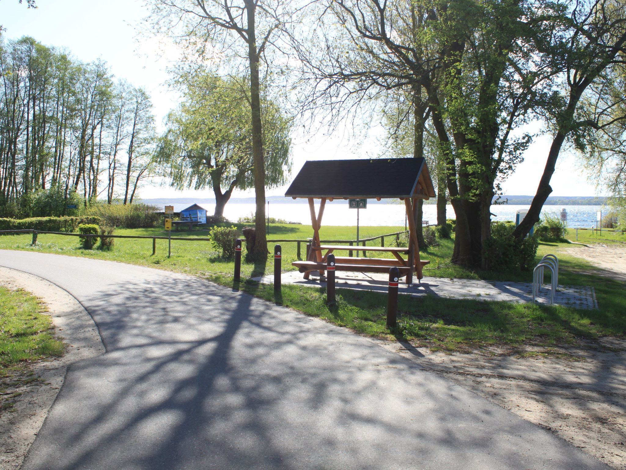 A picnic area with a bench and picnic table, surrounded by trees and a view of a lake.