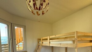 Une chambre avec un lit superposé, une échelle en bois, un matelas blanc et un tapis à motifs.