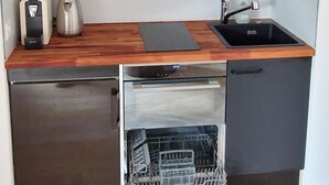 Une cuisine de taille réduite, dotée de meubles de rangement sombres, d’un lave-vaisselle en acier inoxydable, d’un évier et d’une machine à café.