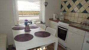 Et køkken med et hvidt bord, lilla underlag, en kaffemaskine og en komfur.