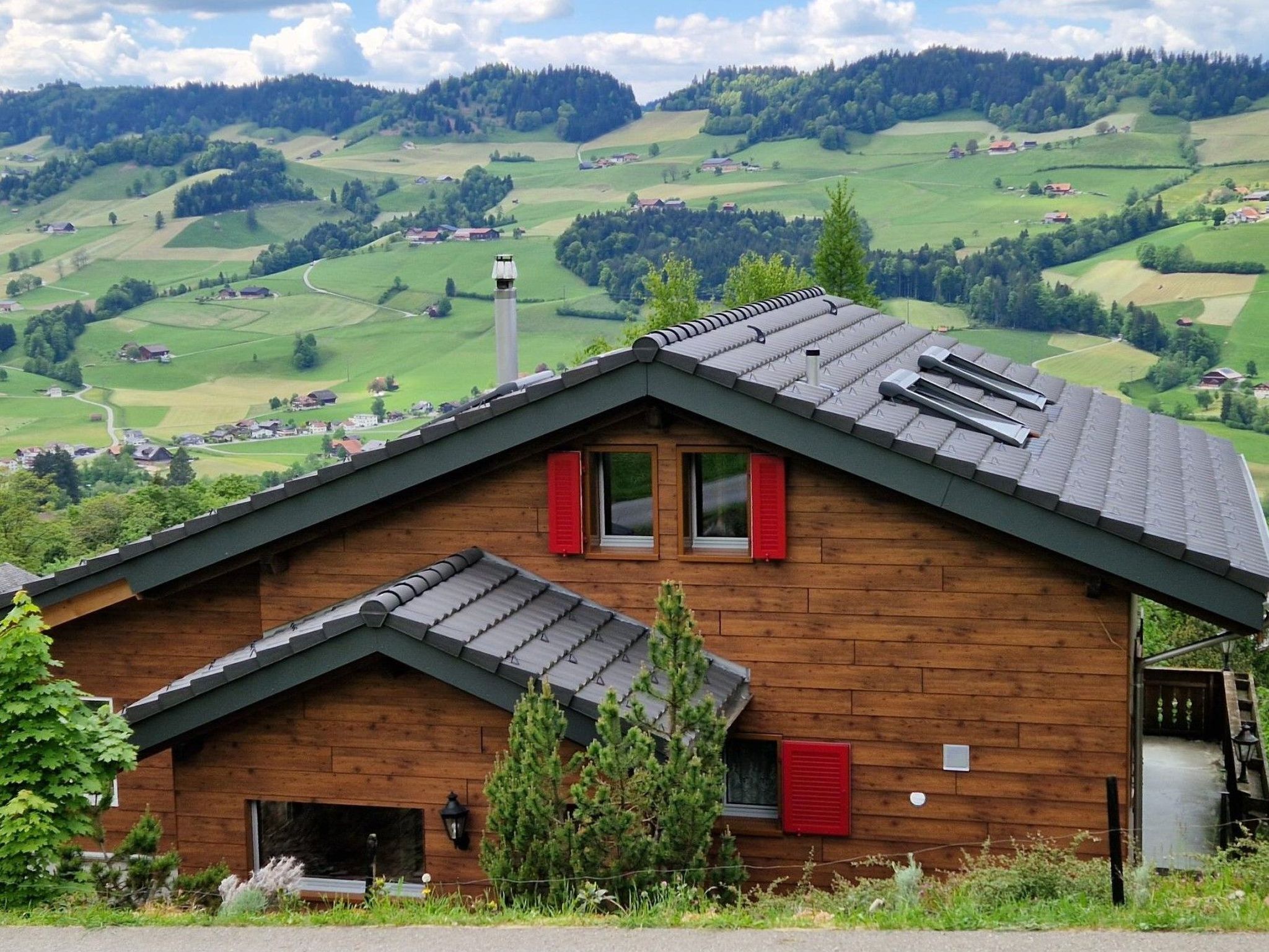 Une cabane en bois avec un toit en pente, des volets rouges et une vue sur une vallée verdoyante.