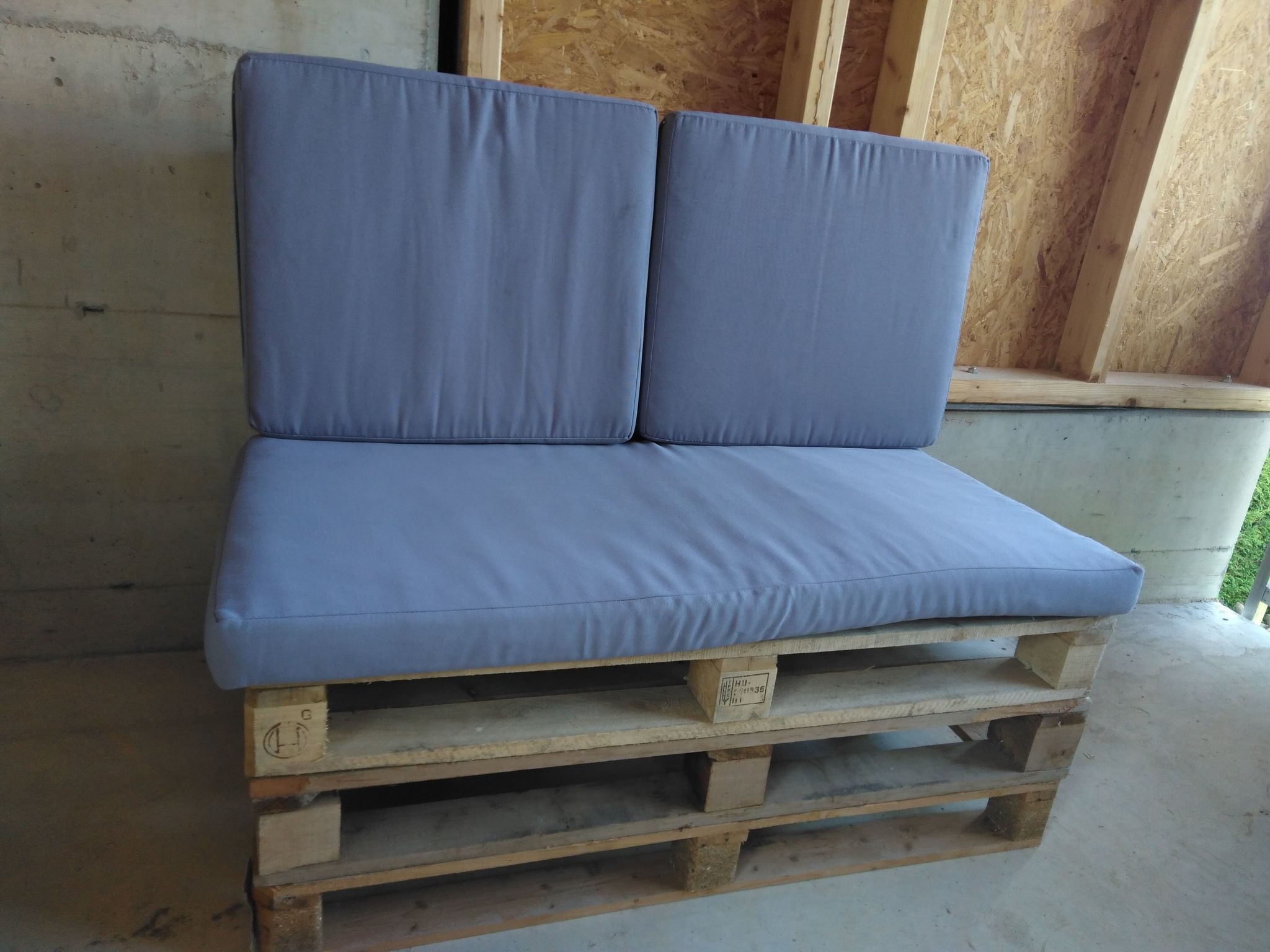 Eine blaue, gepolsterte Sitzbank aus Holzpaletten.