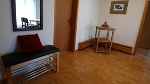Habitació amb una banca de fusta, un mirall, una porta, una taula petita amb una pintura i un radiador.