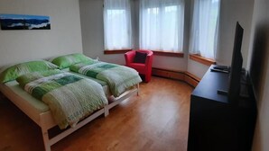 Un dormitori amb un llit, una cadira vermella, un televisor i una finestra amb cortines.