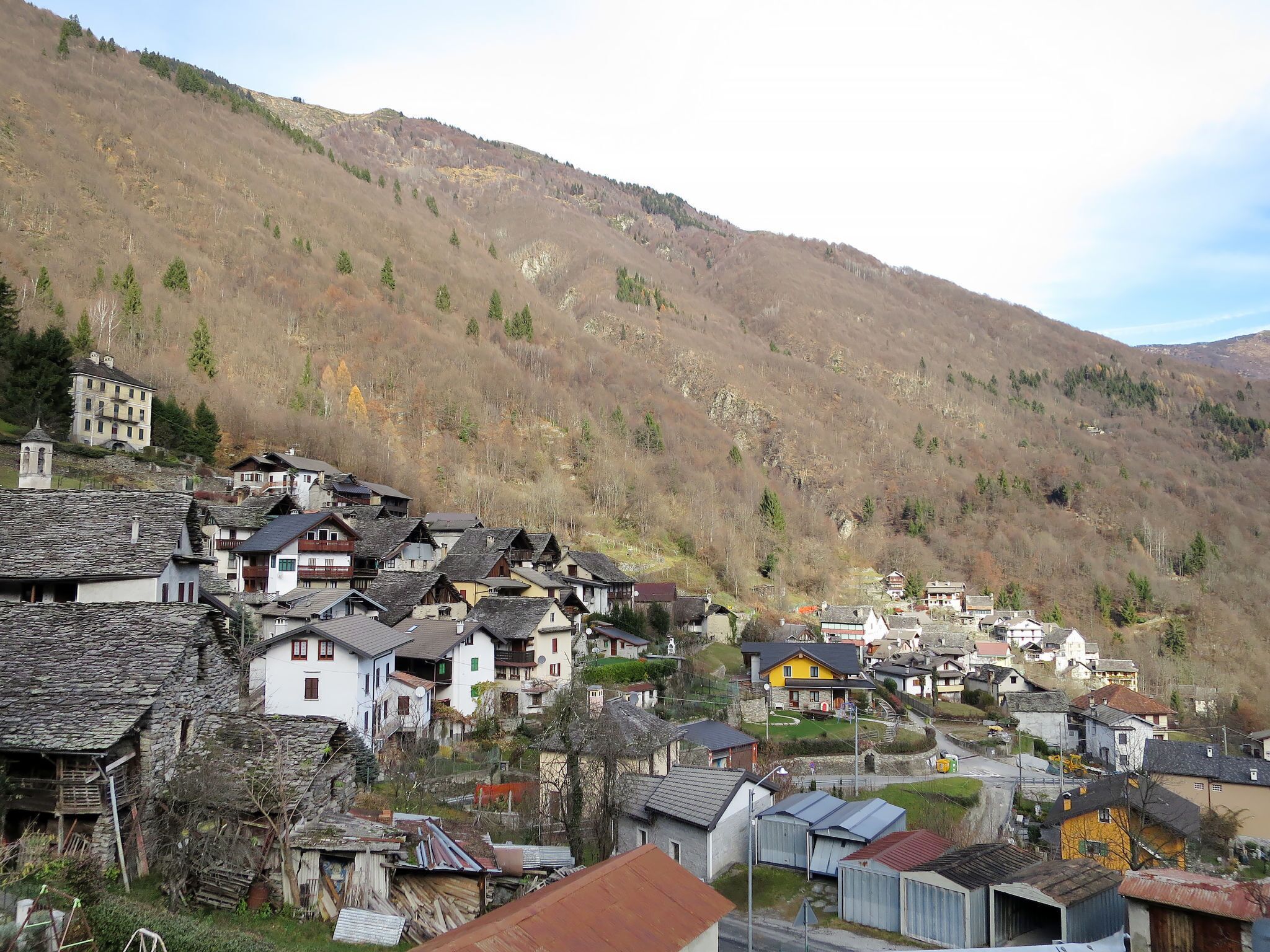 Ein Dorf mit traditionellen Häusern aus Stein und Holz, einer Kirche und einer Hügelkulisse im Hintergrund.
