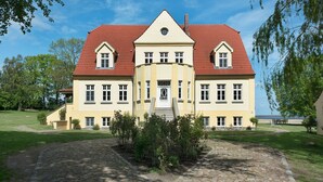 Kaksikerroksinen rakennus, jossa on punatiilestä tehty katto, keskellä sijaitseva sisäänkäynti, jossa on portaikko, sekä symmetrinen julkisivu, jossa on useita ikkunoita.