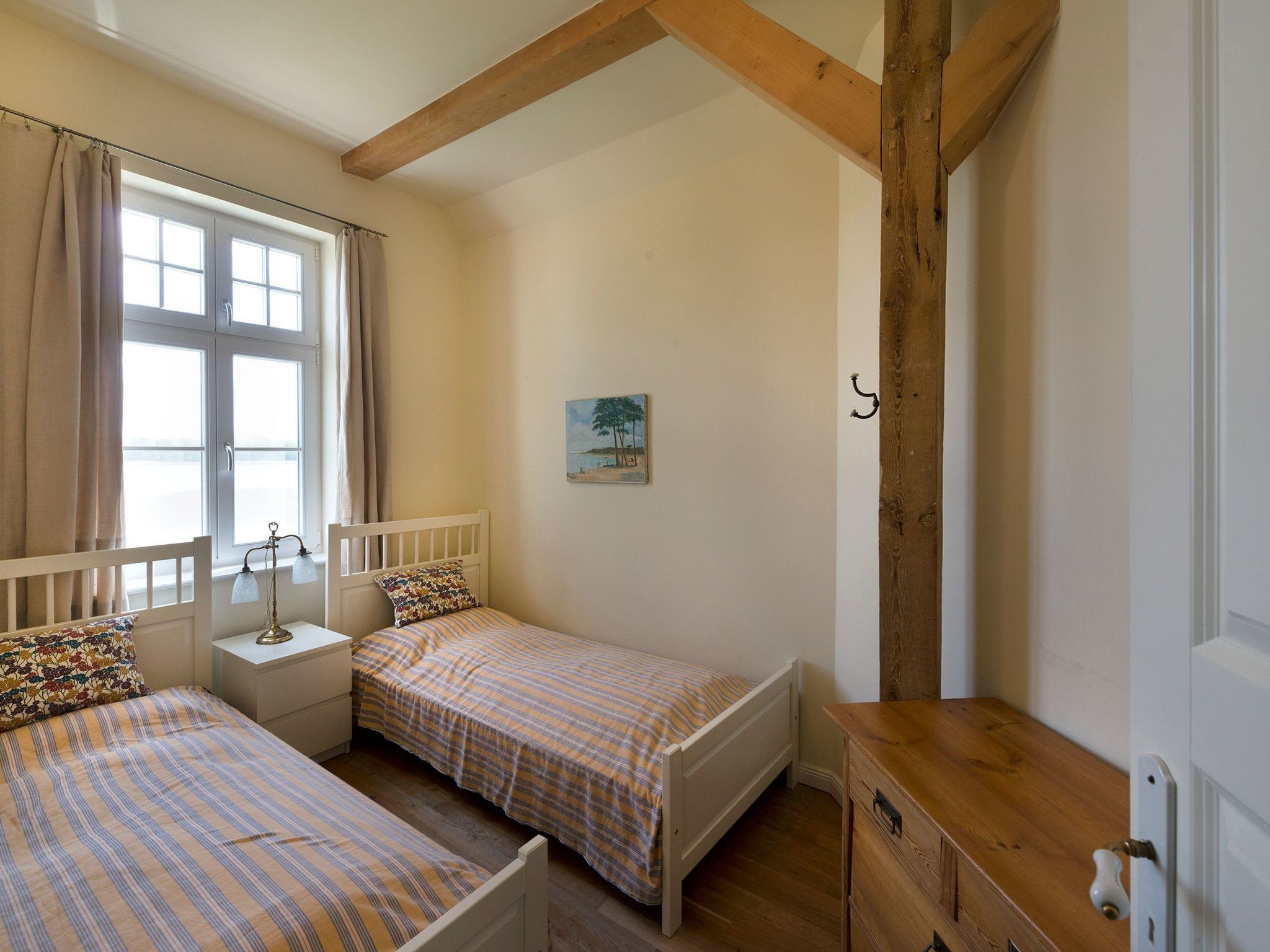 A bedroom with two beds, a wooden dresser, a nightstand, a lamp, and a painting on the wall.