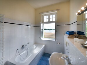 A bathroom with a bathtub, a sink, and a window with a view of a lake. - Wohnung im zweiten Obergeschoss des Gutshauses by Interhome (Gingst)