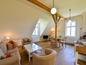 A spacious loft apartment with a high ceiling, exposed wooden beams, a dining area, a living room with a sofa and armchairs, and a kitchen with modern appliances. - Wohnung im zweiten Obergeschoss des Gutshauses by Interhome (Gingst)