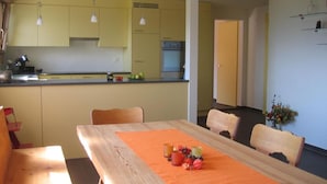 Eine kompakte Küche mit gelben Schränken, einer zentralen Kochinsel und einem Essbereich mit Holztisch und Stühlen.
