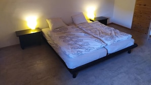 Ein Schlafzimmer mit Holzbalkendecke, einem Bett mit gemusterten Betttextilien sowie zwei Nachttischen und Nachttischlampen auf jeder Seite.