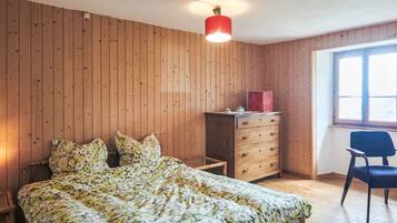 Ein Schlafzimmer mit einer holzgetäfelten Wand, einem Bett mit Blumenmuster auf der Bettwäsche, einem Schminktisch, einem Stuhl und einem Fenster.