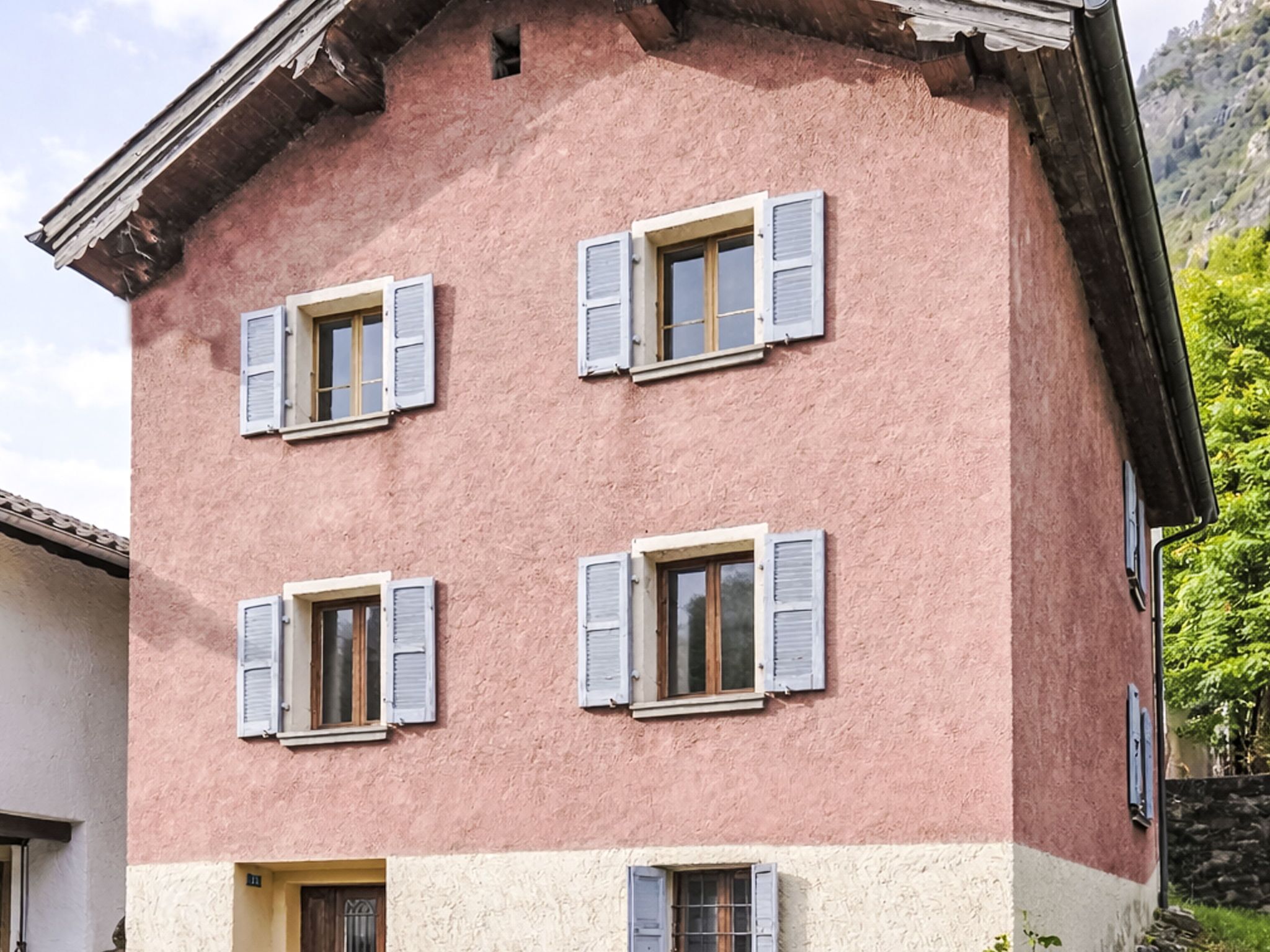 Ein mehrgeschossiges Gebäude mit vier Fenstern, jeweils mit Fensterläden, und einem flachen Dach.