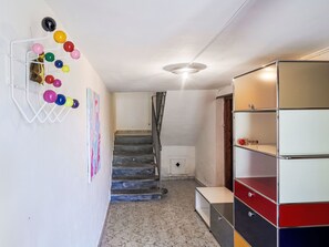 A hallway with a staircase, a wall-mounted rack with colorful balls, and a multi-tiered storage unit. - Waterfall House by Interhome (Mesocco)