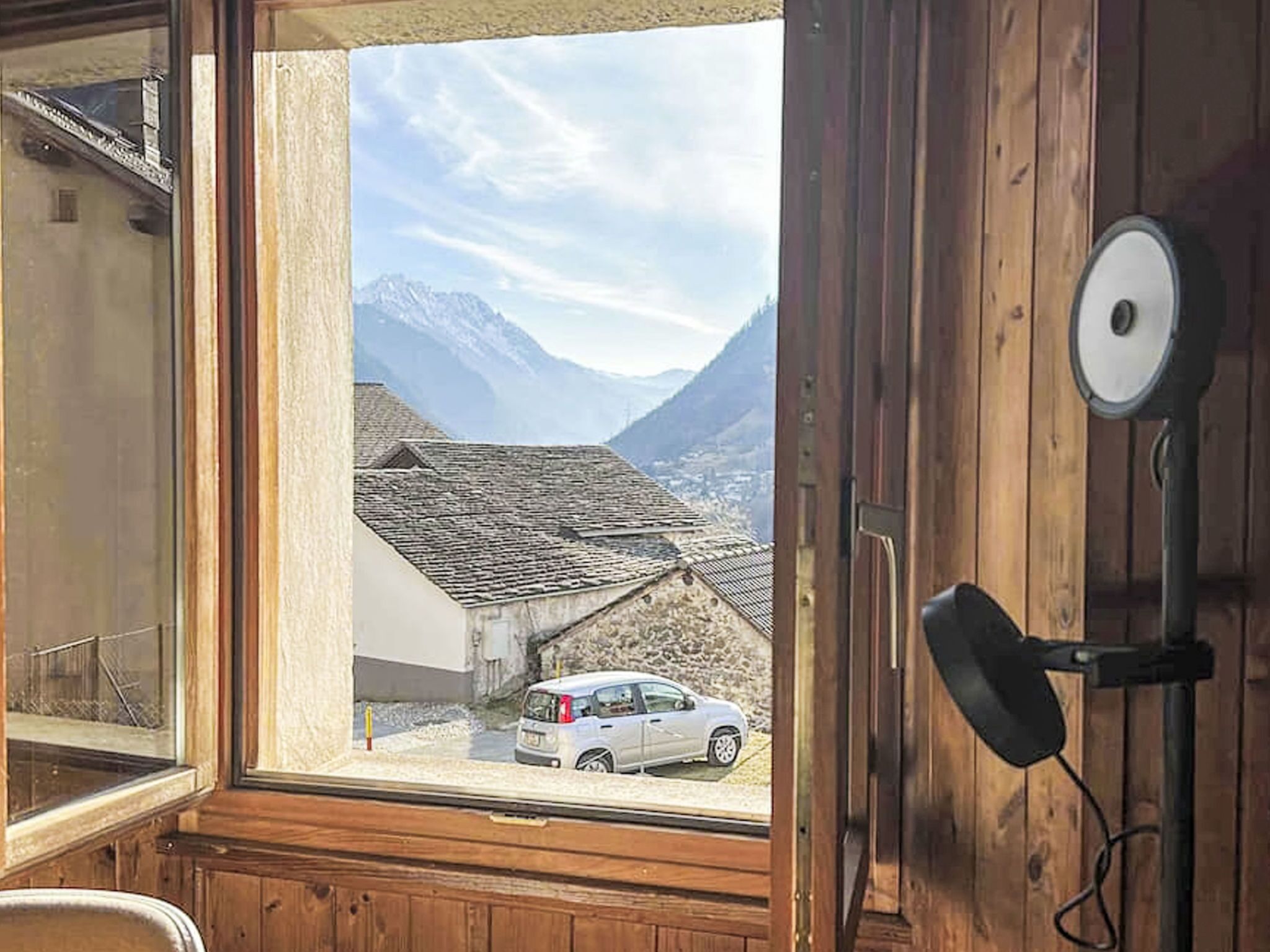 Quarto com decoração em madeira, janela com vista para uma paisagem montanhosa e um carro branco estacionado na parte externa.