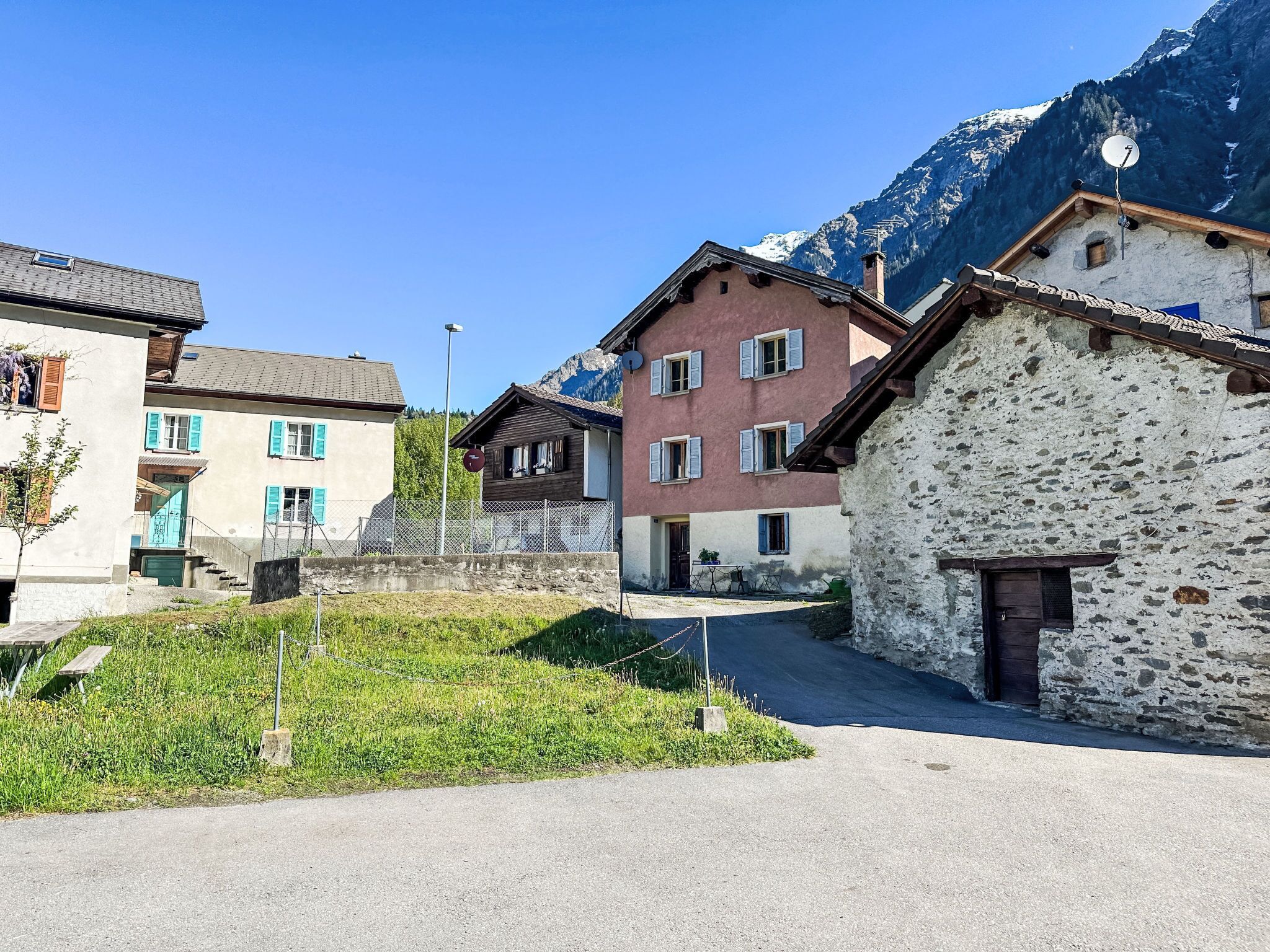 Eine ländliche Straße mit traditionellen Gebäuden, blauem Himmel und Bergen im Hintergrund.