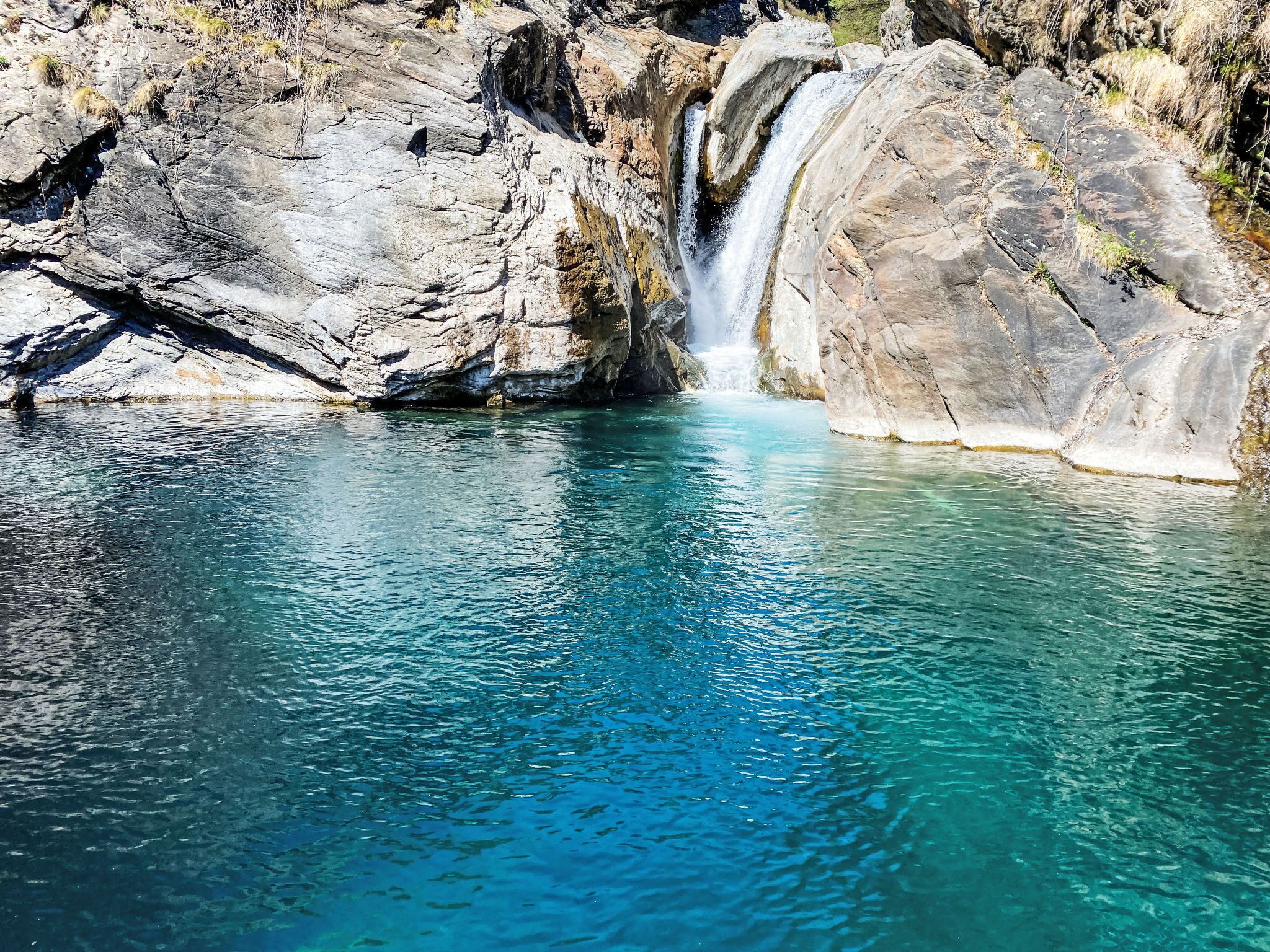 Een helderblauw zwembad met een waterval die naar beneden stroomt over een rotswand.