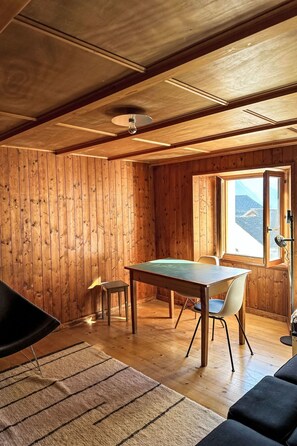 A wooden interior with a dining table, chairs, a sofa, and a window with a view.