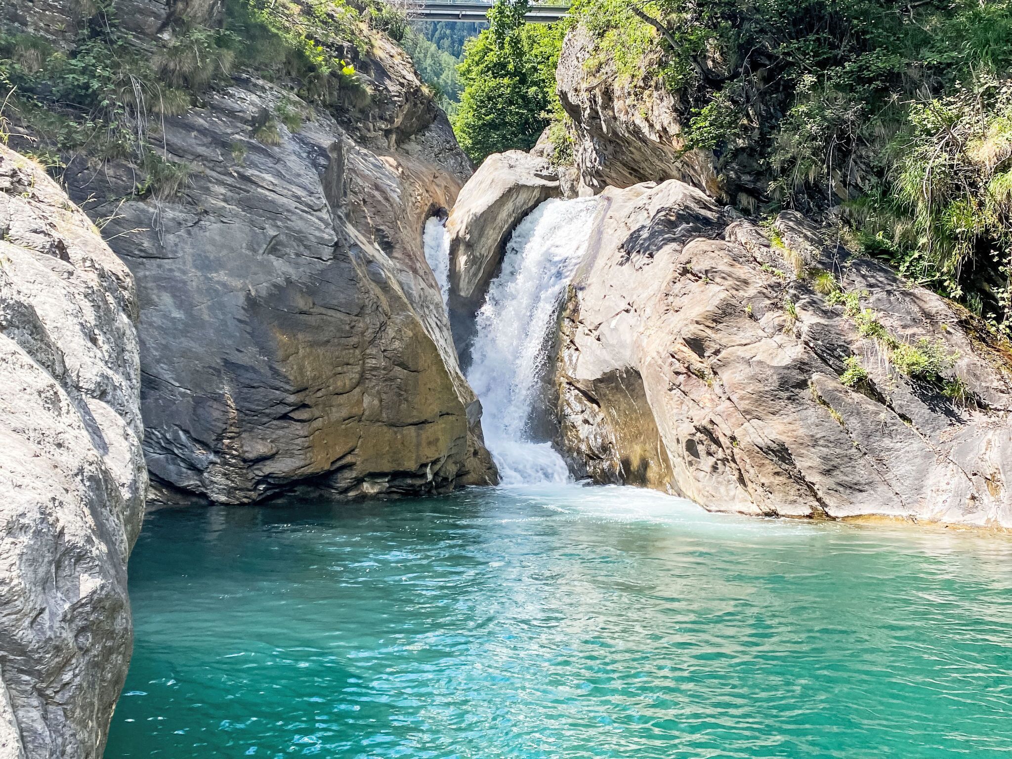 A waterfall cascading into a clear turquoise pool surrounded by rocky terrain and greenery.