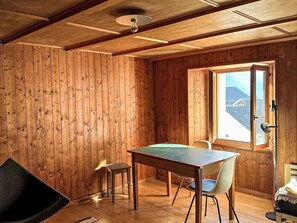 A wooden room with a table and chairs, a window with a view, and a ceiling fan. - Waterfall House by Interhome (Mesocco)