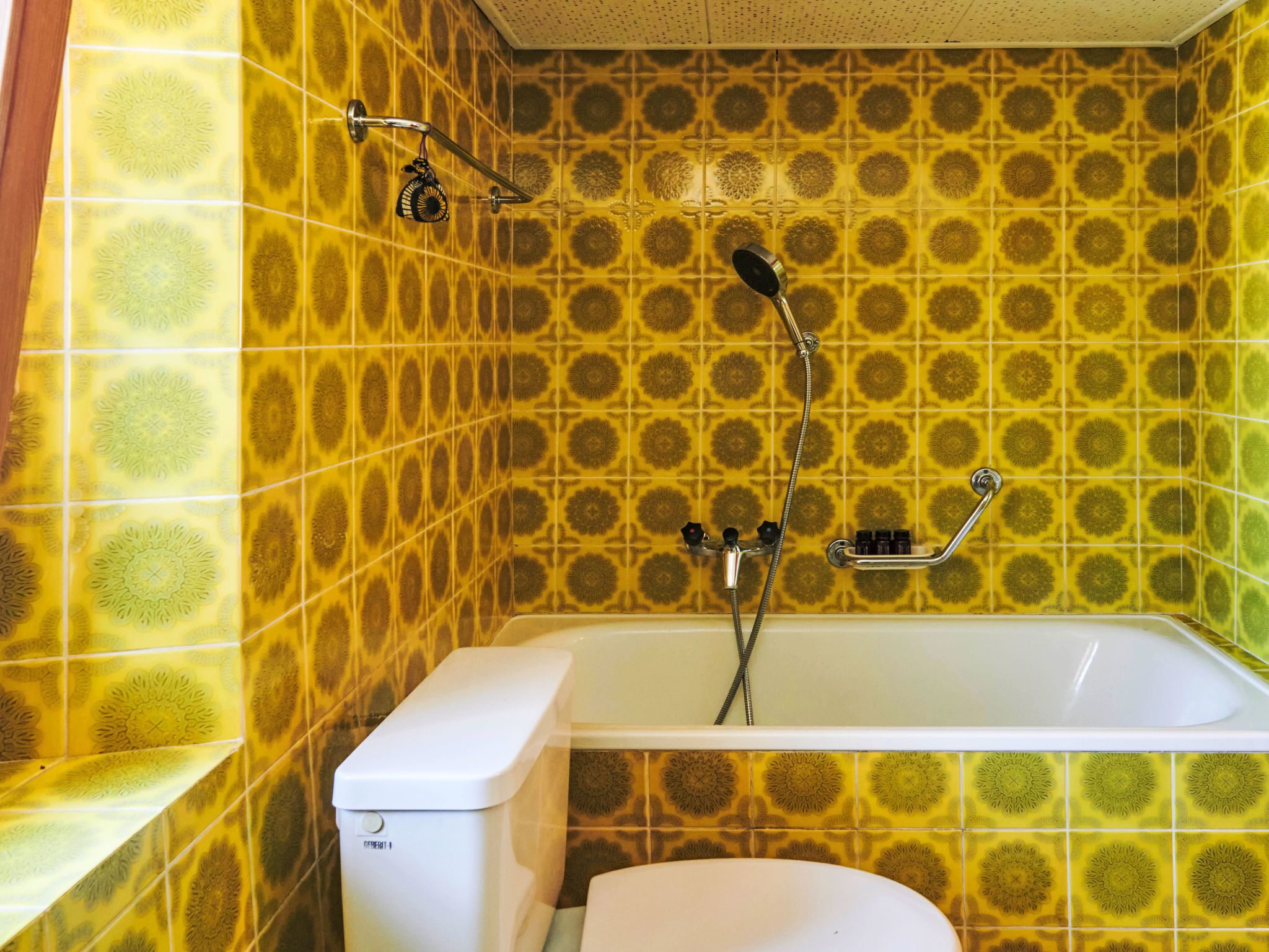 Un bagno con piastrelle gialle decorate, una vasca da bagno bianca e un water bianco.