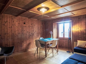 A wooden interior with a dining table, chairs, a sofa, and a window.