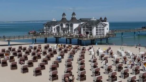 Ein Strandhotel mit Liegestuhlreihen und einem Steg, der ins Meer führt.